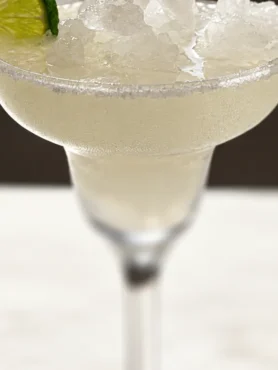 Cloudy margarita with crushed ice, a salted rim and lime wheel.
