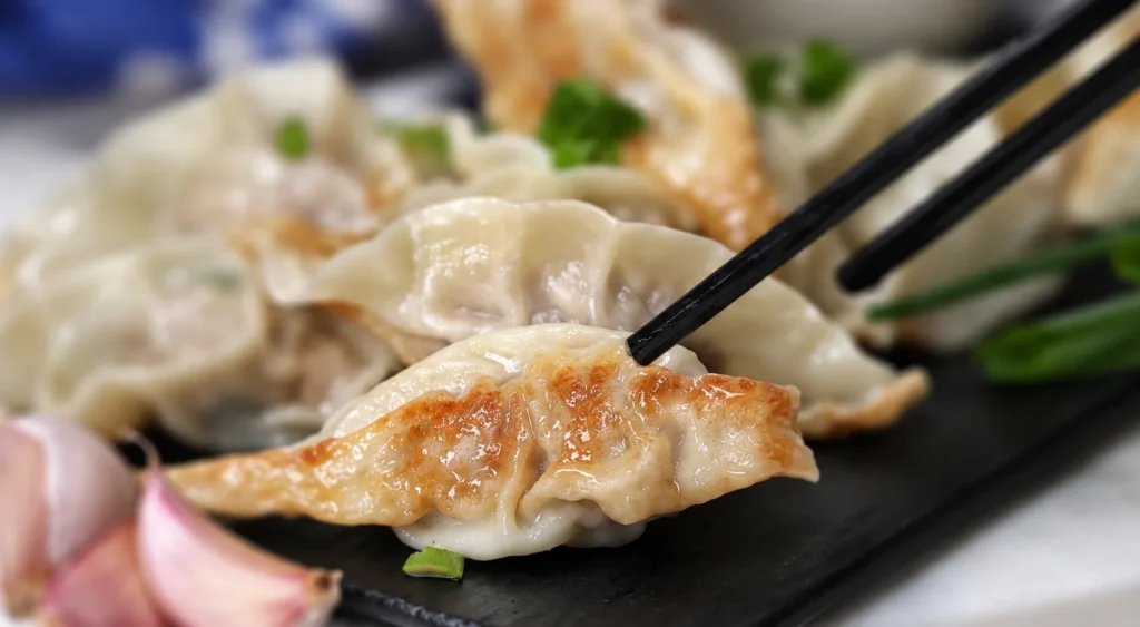 A browned soup dumpling held by chopsticks above a dark plate.