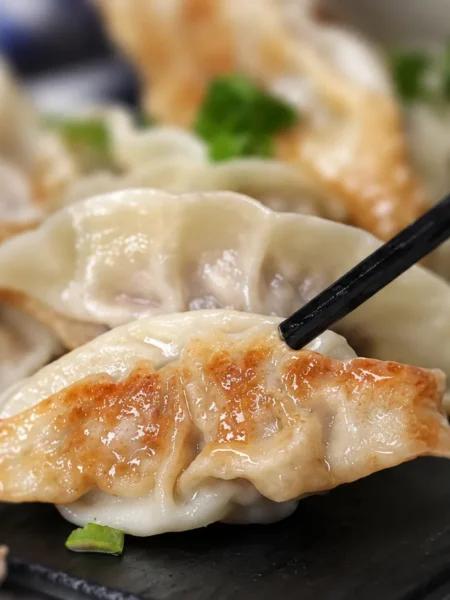 A browned soup dumpling held by chopsticks above a dark plate.