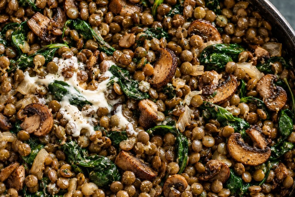 Green lentils with browned mushrooms, wilted spinach and crème fraîche in a dark pan.