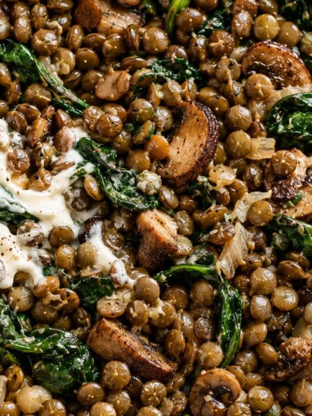Green lentils with browned mushrooms, wilted spinach and crème fraîche in a dark pan.